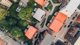 Top-down dronebillede af moderne byhuse med orange og lyse tage omgivet af grønne arealer – fotograferet af Kasper Hornbæk