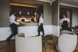 Travl service i åben køkkenlounge med kokke i fuld gang og tjenere i bevægelse – eksklusiv restaurantstemning med stilrent interiør.