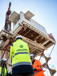 Innargi-medarbejdere i dialog under stor borestruktur, set nedefra med tydeligt firmalogo på arbejdstøjet.