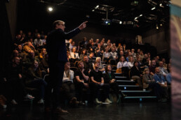Mand peger engageret mod publikum under præsentation i fyldt foredragssal til Klean Groups AI-arrangement.