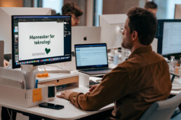 Mand arbejder ved skrivebord med en præsentation på skærmen, hvor der står 'Mennesker før teknologi' – et motto fra Klean Group.