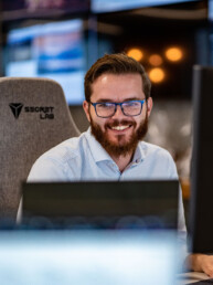Portræt af smilende medarbejder hos Klean Group, omgivet af computerskærme i et moderne kontormiljø.