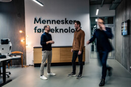 Kollegaer i samtale foran væg med teksten 'Mennesker før teknologi' i Klean Groups kontor.