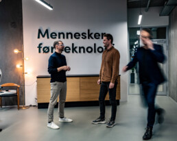 Kollegaer i samtale foran væg med teksten 'Mennesker før teknologi' i Klean Groups kontor.