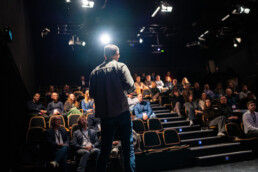 Mand holder oplæg foran et fokuseret publikum i en mørklagt teatersal, under Klean Groups AI-event.