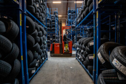Gaffeltruck kører gennem lagergang med stablede vinterdæk hos NDI. Industrielt dæklager med høj effektivitet.
