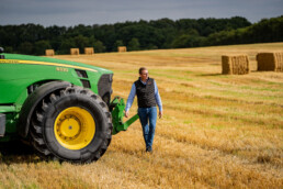 Mand ved John Deere traktor i høstklar mark med halmballer i baggrunden. Landbrug og dækløsninger til store maskiner.
