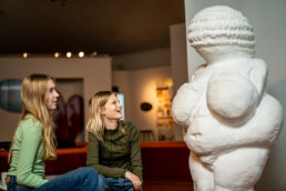 To piger smiler og kigger på en skulptur i udstillingen Venus fra Willendorf på Science Museerne i Aarhus.