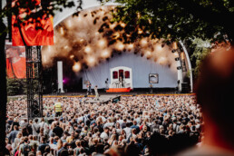 Panoramaudsigt af scenen på Smukfest, tæt pakket publikum og energisk optræden med scenelys. Foto taget af Kasper Hornbæk.