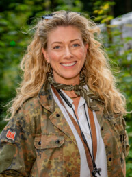 Smilende kvinde med krøllet hår og camouflagejakke ved Smukfest. Portræt med naturlig baggrund fotograferet af Kasper Hornbæk