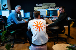 Udviklere i dialog foran computerskærme – tech virksomhed med fokus på innovation og samarbejde.